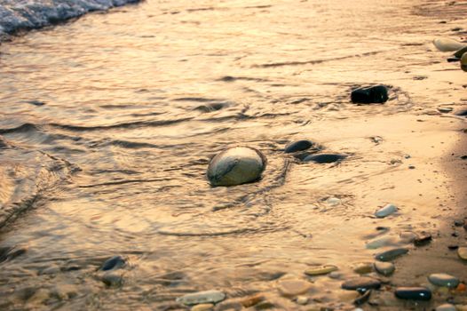 stones at sea shore covered with film of flowing water at sunset