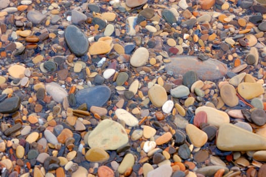 closeup of sea shore with pebbles covered with film of water