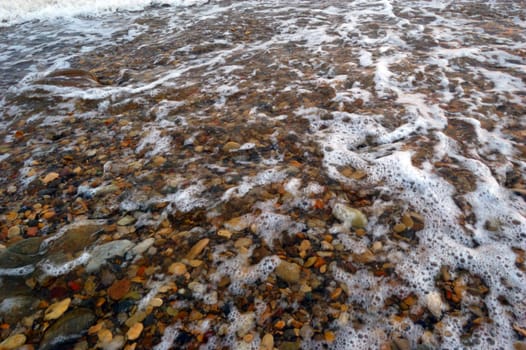 closeup of sea shore with pebbles covered with film of water