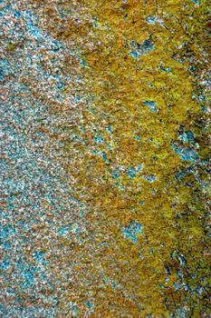colored (prevaling yellow and blue) rough stone surface with lichen