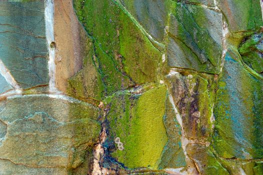 colored (prevaling green) rough wall surface made of wild stones with lichen