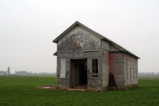 An old one room school house in a field on a cloudy day.