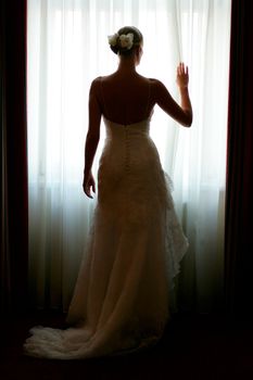 Silhouette of a beautiful bride in a traditional white wedding dress, stood by window.