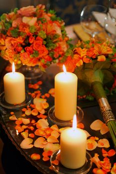 Romantic burning candles and scattered flower petals on table.