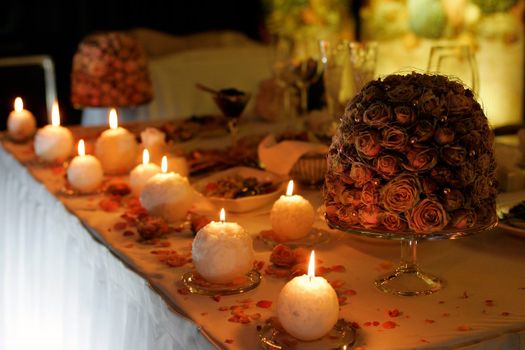 Romantic burning candles and scattered flower petals on table.