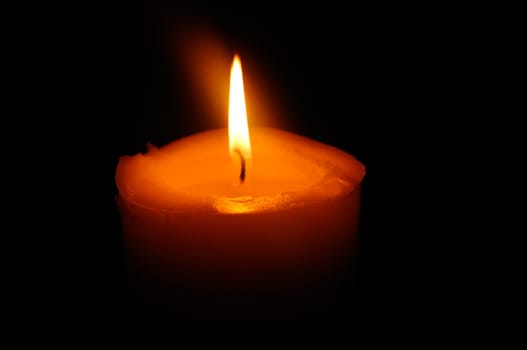 Solitary orange candle shining in the darkness.