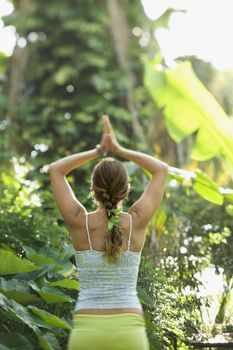 Rear view of Caucasian mid-adult woman holding arms overhead in yoga position.