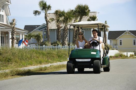 Caucasian mid-adult man and woman driving golf cart down residential street.