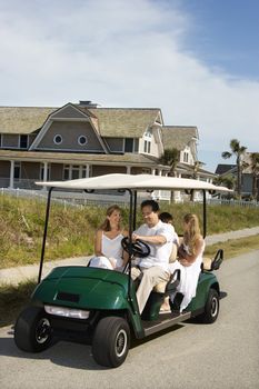 Caucasian family of four driving golf cart down residential street.