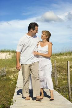 Caucasian mid-adult couple holding each other walking down beach access path.