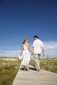 Caucasian mid-adult couple holding hands walking down beach access path.
