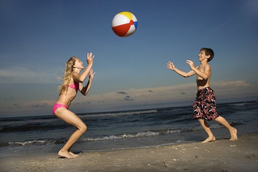 Caucasian pre-teen girl and boy playing with beachball on beach.