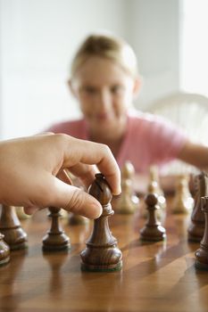 Caucasian hand moving chess piece with pre-teen girl watching in background.