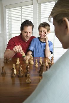 Caucasian mid-adult mother watching mid-adult dad teaching chess to pre-teen son.