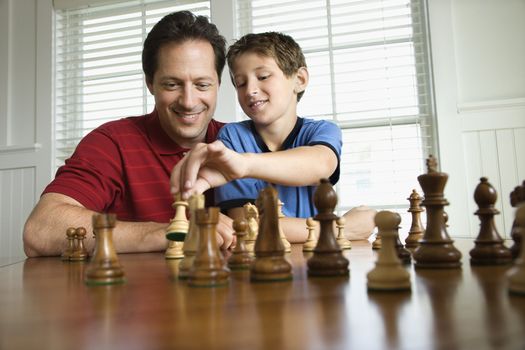 Caucasian mid-adult dad teaching chess to pre-teen boy.