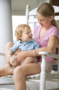 Caucasian pre-teen girl holding male Caucasian toddler looking at each other.