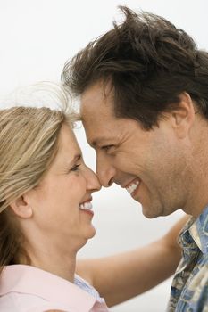 Caucasian mid-adult man and woman holding each other and looking into each other's eyes on beach.