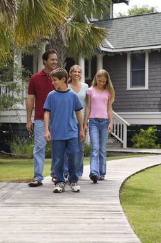 Caucasian family of four walking down suburban sidewalk with house in background.