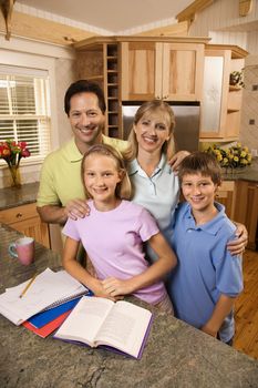 Caucasian family of four standing in kitchen posing with homework on counter.