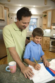 Caucasian mid-adult father helping pre-teen son with homework in kitchen.