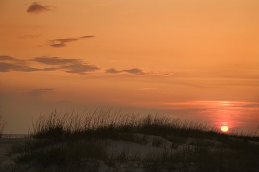 Sun setting over beach sand dune on Bald Head Island, North Carolina.
