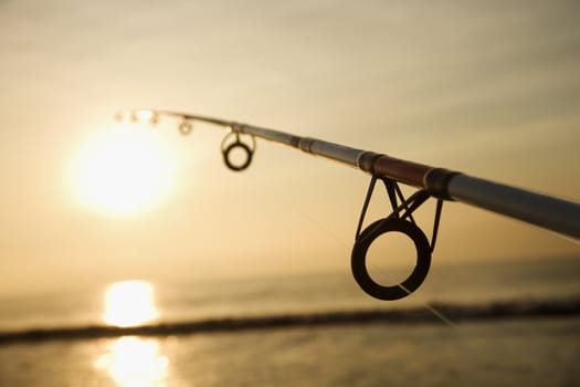 Fishing pole against ocean at sunset.