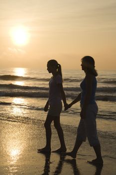 Caucasian prime adult female and female child walking on beach at sunset holding hands.