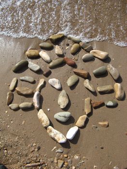 african mask drawed with pebbles on the beach