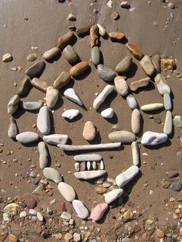 african mask drawed with pebbles on the beach