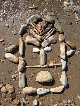 african mask drawed with pebbles on the beach