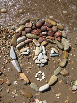 african mask drawed with pebbles on the beach