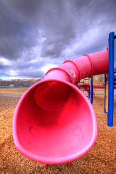 A child's playground set tube slide with wood-chips about on the ground.