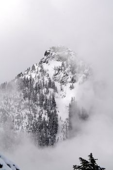 A snow capped mountain peeking from behind its cloud veil.