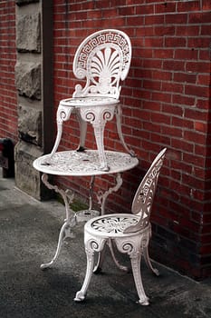 A Victorian style table and chair stacked on the sidewalk.