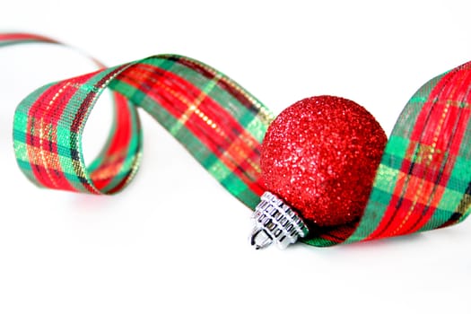 A Christmas ribbon and ornament on a white background. Used a shallow depth of field and selective focus on the cap of the ornament.
