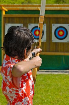 An archer aims at the bullseye of a distant target. Focus on the archer's head. The arrow can just be seen, out of focus, in the bullseye.