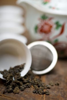 dry green chinese tea set,with strainer closeup,cups and teapot on background over old wood board