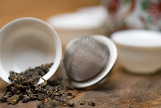 dry green chinese tea set,with strainer closeup,cups and teapot on background over old wood board