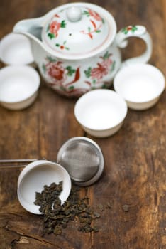 dry green chinese tea set,with strainer closeup,cups and teapot on background over old wood board