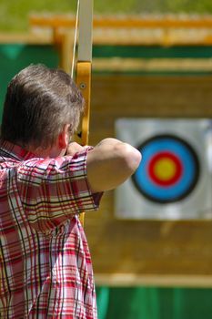 An archer aims at the bullseye of a distant target. Selective focus on the archer's head.