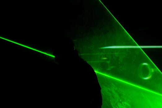 Silhouette of a man playing guitar surrounded by green lasers.