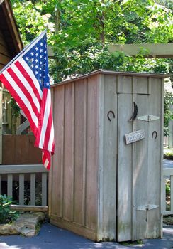 A flag along side an old fashion outhouse.
