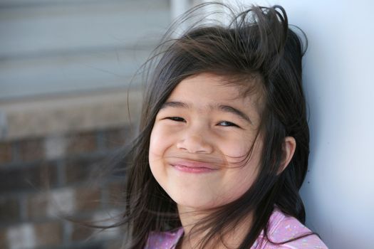 Happy six year old girl standing against wall outdoors