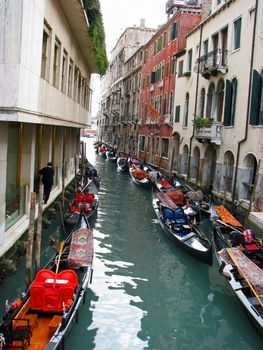 Venice canal with gondolas and individual walking on the edge.
