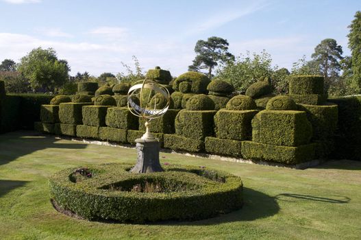 A sun dial in a formal garden with  hedging in the background