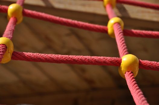 Climbing ropes construction on playground - red ropes with yellow elements and blurred backround
