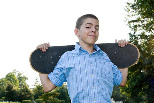 A boy in his early teens happily standing with his skateboard.