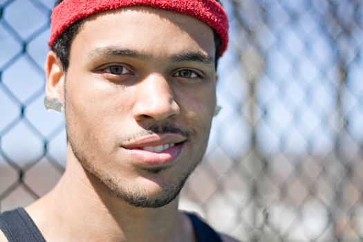 A basketball player posing at the park outdoors in front of a chain linked fence.