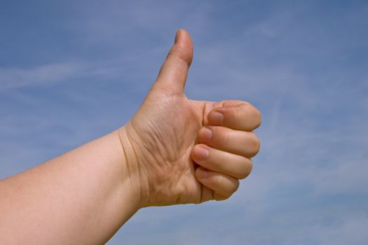 Fist with a thumb up against blue sky