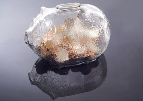 a glass piggy bank with coins  feflecting on a water base background